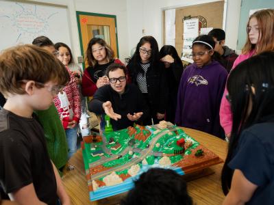 Image of teacher surrounded by students, as they are all focused on a simulation.